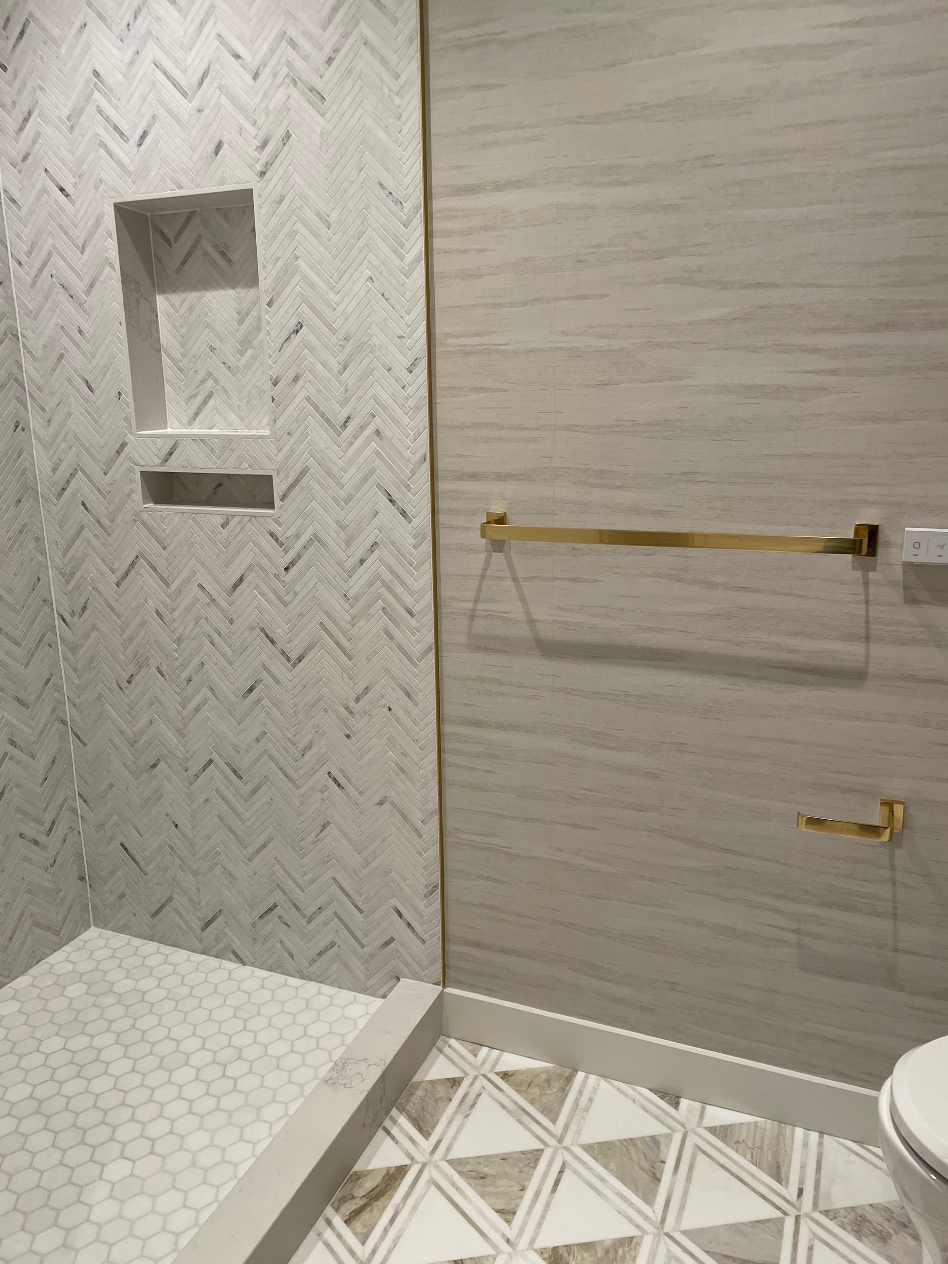 Walk-in shower with herringbone marble walls, brass accents, and geometric floor tile