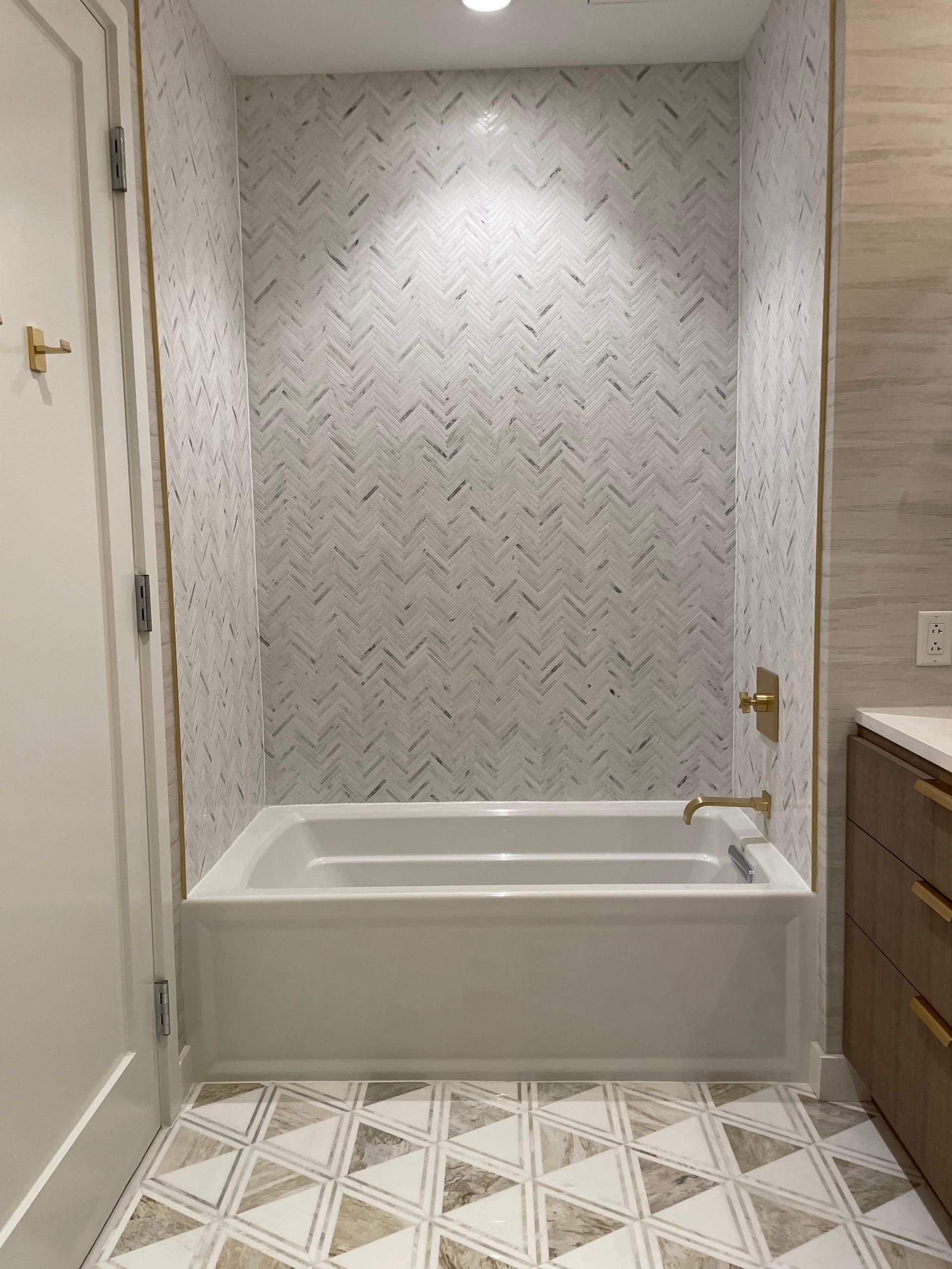 Built-in soaking tub alcove with marble herringbone wall tile and brass fixtures